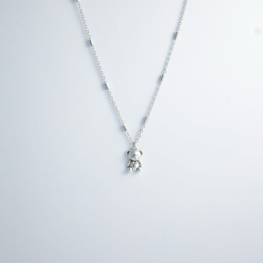 Dainty silver bar link chain with a teddy bear charm for minimalistic fashion or for layering jewelry on a light gray background