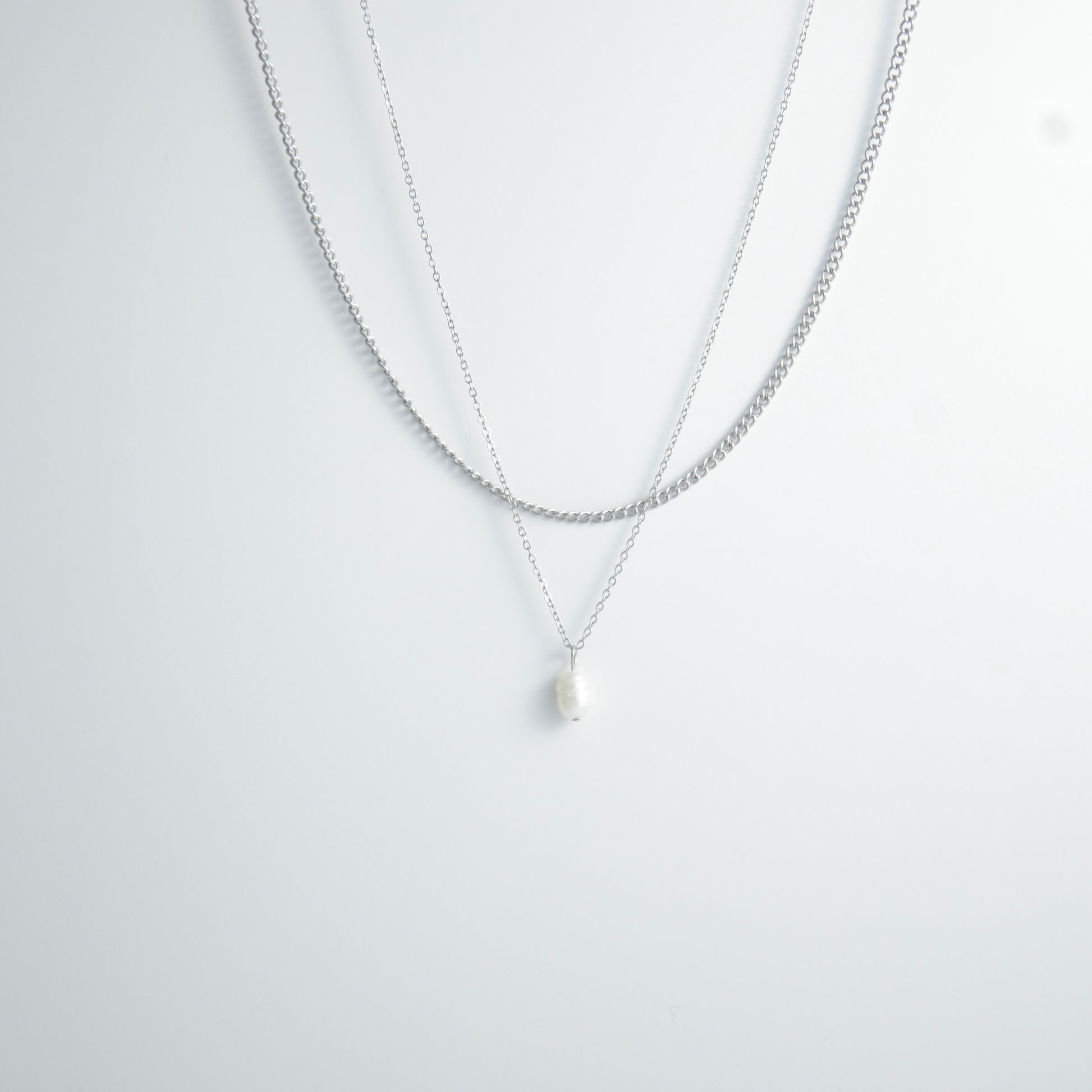 Silver stainless steel layered necklace set with a curb chain and a dainty pearl pendant necklace on a light gray background
