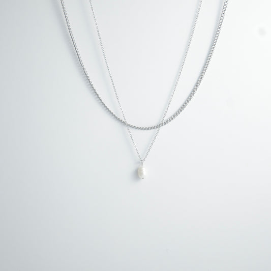 Silver stainless steel layered necklace set with a curb chain and a dainty pearl pendant necklace on a light gray background
