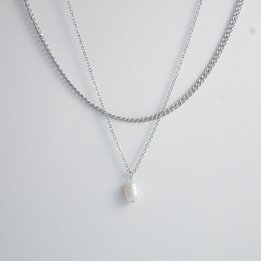 Silver stainless steel layered necklace set with a curb chain and a dainty pearl pendant necklace on a light gray background