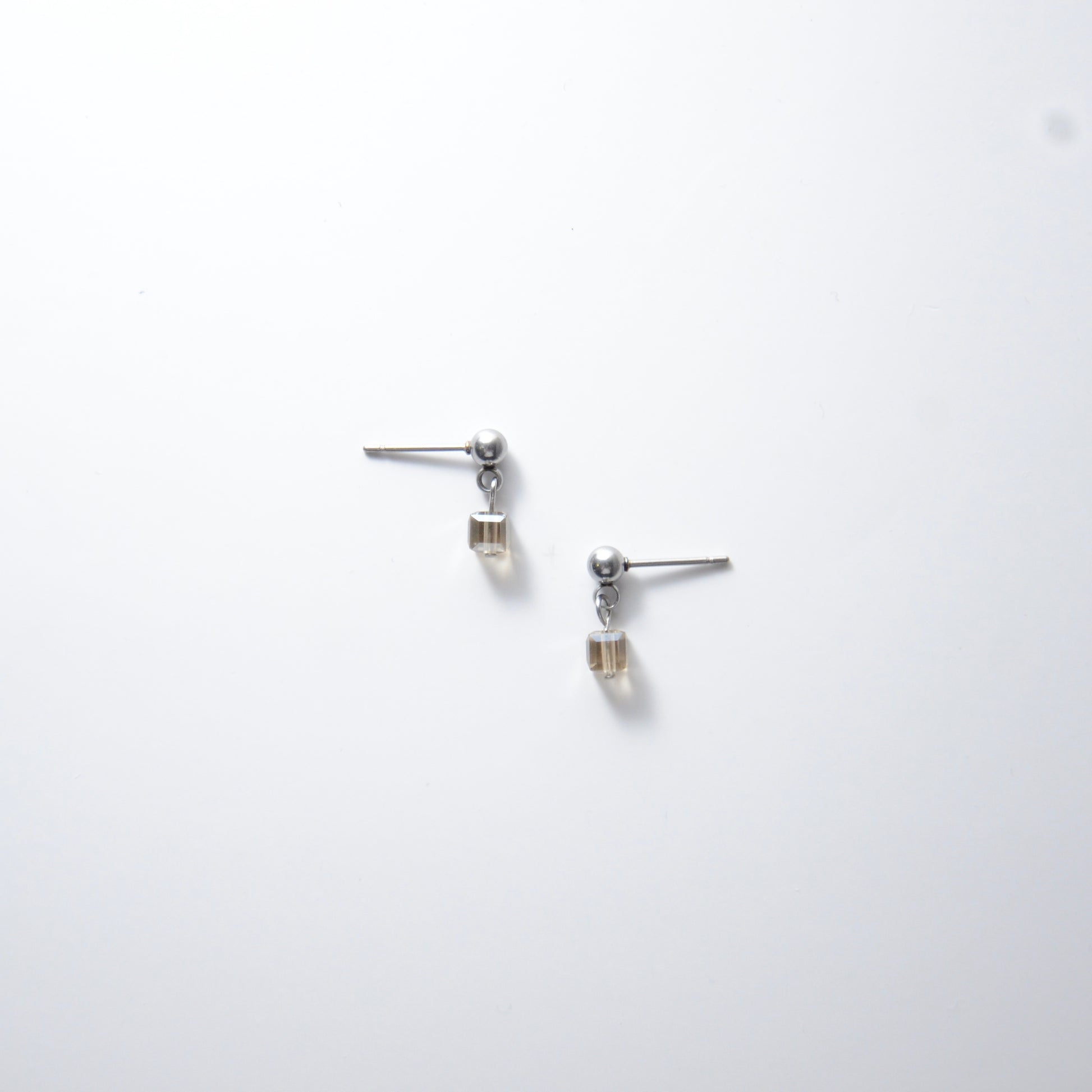 Pair of silver stainless steel ball stud earrings with sugar cube gray glass beads on a white background