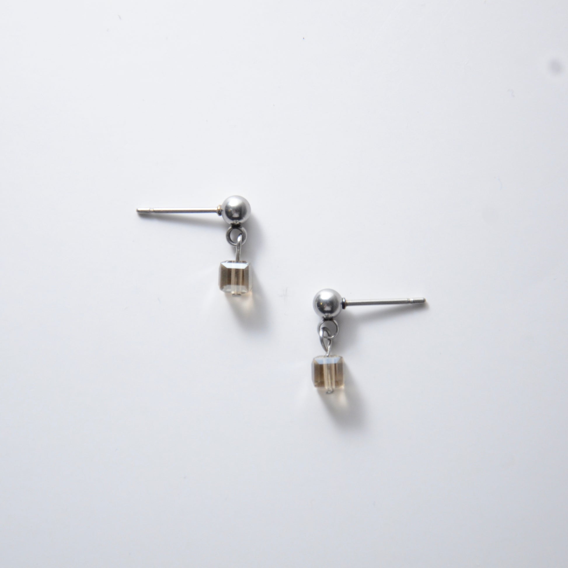 Pair of silver stainless steel ball stud earrings with sugar cube gray glass beads on a white background