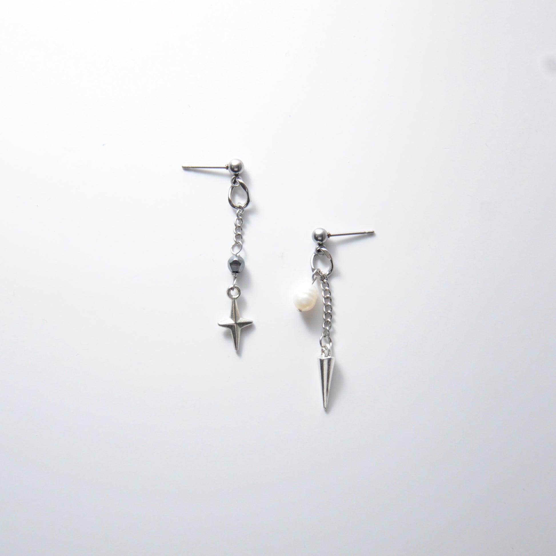Pair of silver stainless steel ball stud drop earrings with a chain and star charm and a pearl and spike charm on a white background