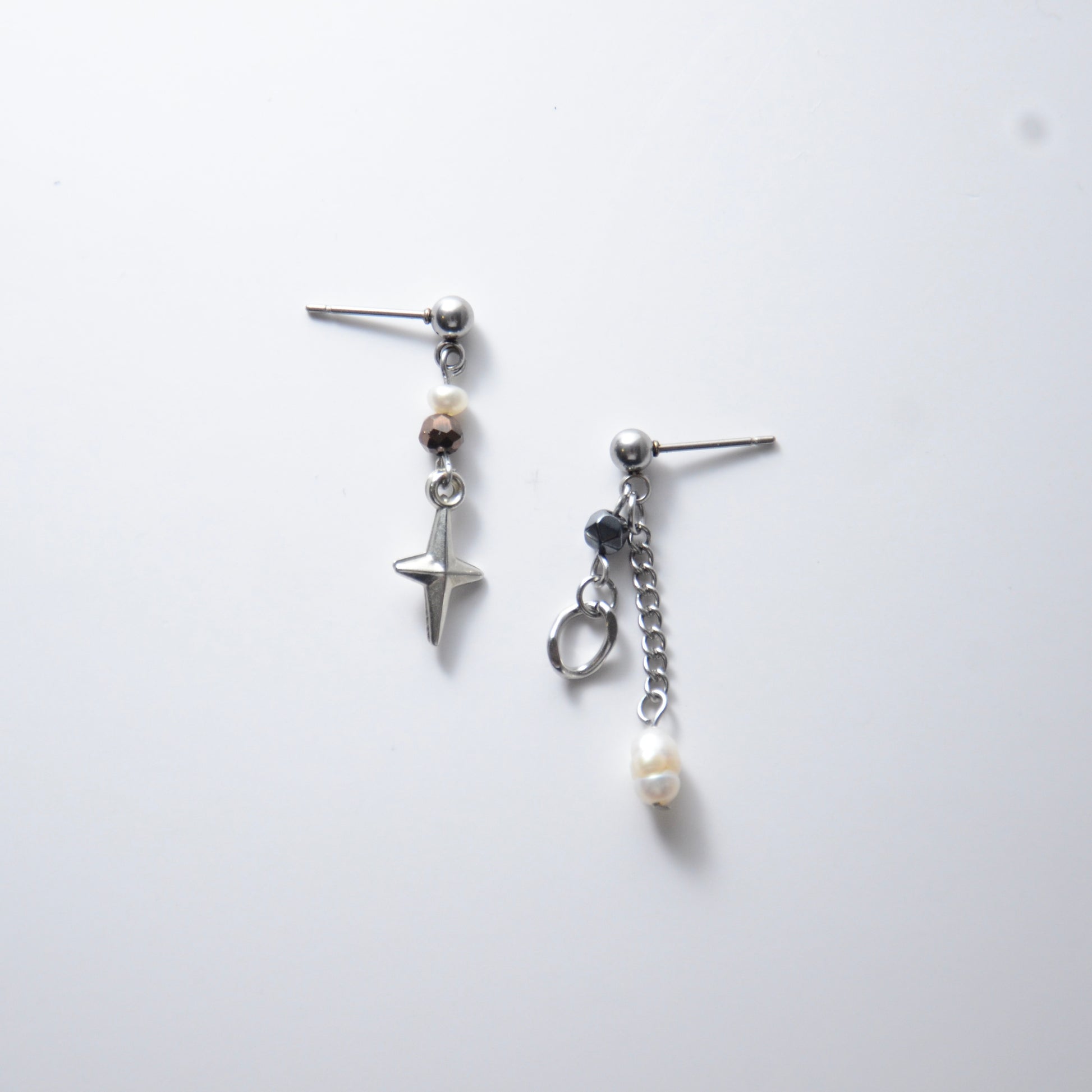 Pair of silver stainless steel ball stud drop earrings with orange and black glass beads and star and pearl charm with unique designs on a white background