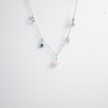 Silver stainless steel delicate charm necklace with small pink, black, purple glass beads and a geometric charm on a light gray background