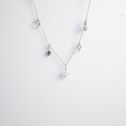 Silver stainless steel delicate charm necklace with small pink, black, purple glass beads and a geometric charm on a light gray background