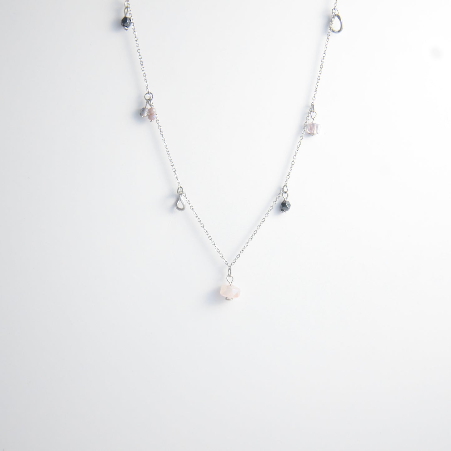 Silver stainless steel delicate charm necklace with small pink, black, purple glass beads and a geometric charm on a light gray background