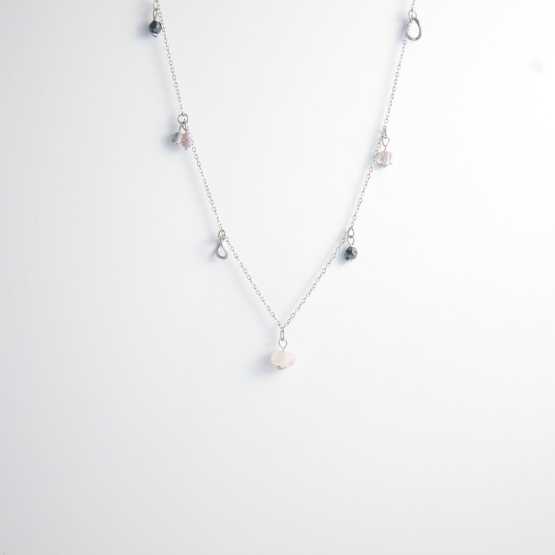 Silver stainless steel delicate charm necklace with small pink, black, purple glass beads and a geometric charm on a light gray background