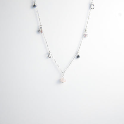 Silver stainless steel delicate charm necklace with small pink, black, purple glass beads and a geometric charm on a light gray background