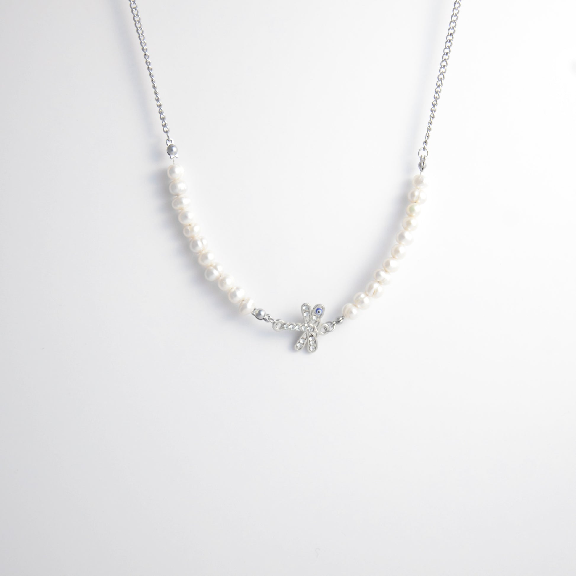 Silver stainless steel pearl choker necklace with a silver dragonfly evil eye pendant on a light gray background