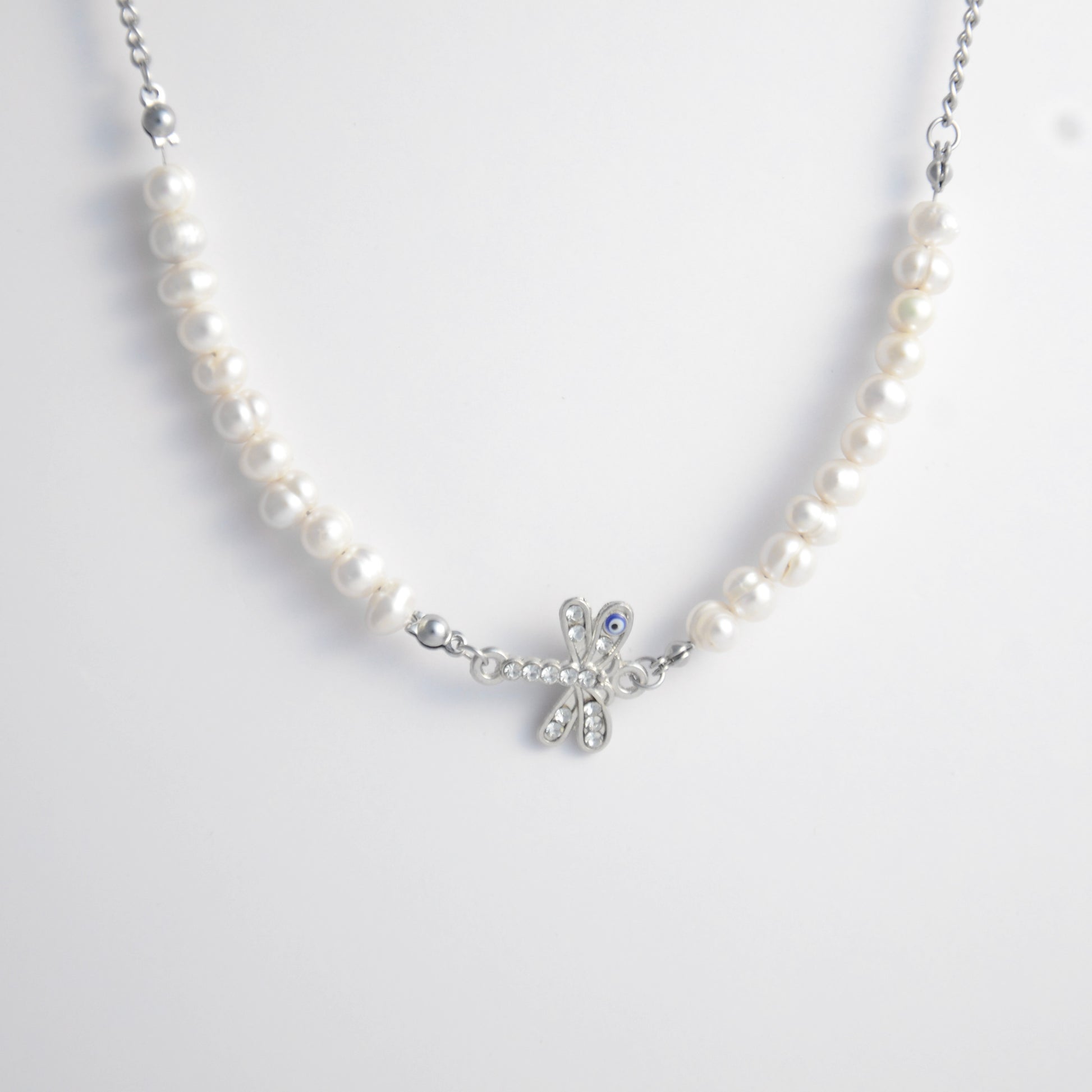 Silver stainless steel pearl choker necklace with a silver dragonfly evil eye pendant on a light gray background
