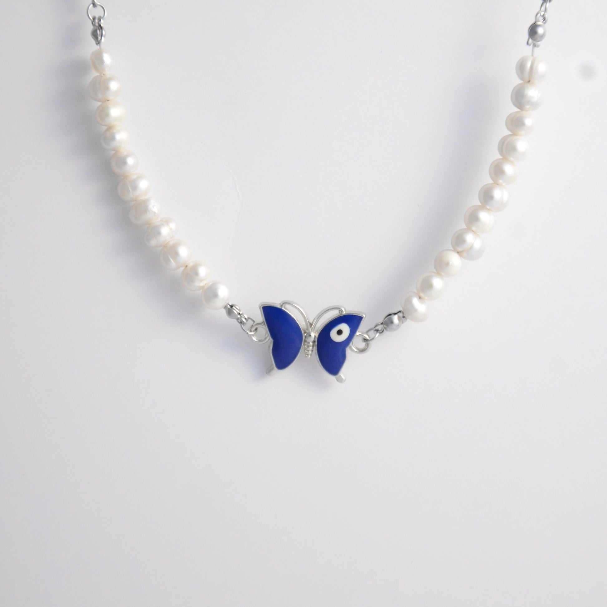 Silver stainless steel pearl choker necklace with a blue butterfly evil eye pendant on a light gray background
