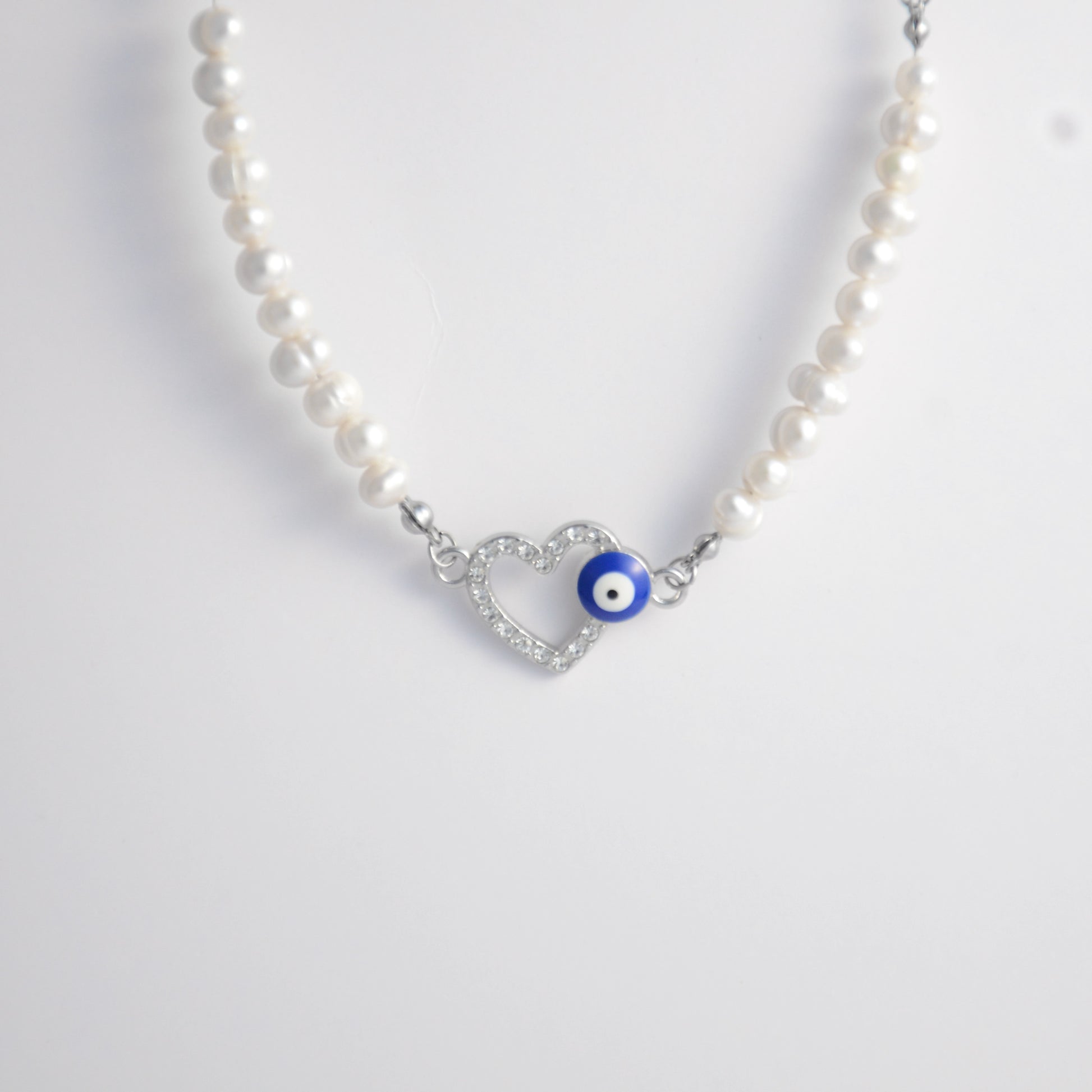 Silver stainless steel pearl choker necklace with a silver heart evil eye pendant on a light gray background