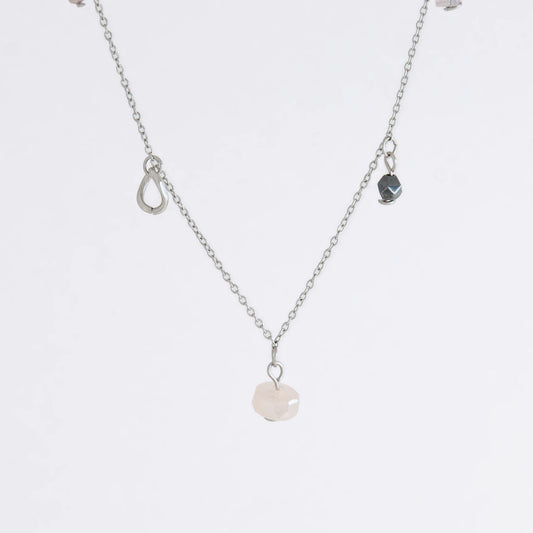 Silver stainless steel delicate charm necklace with small pink, black, purple glass beads and a geometric charm on a light gray background