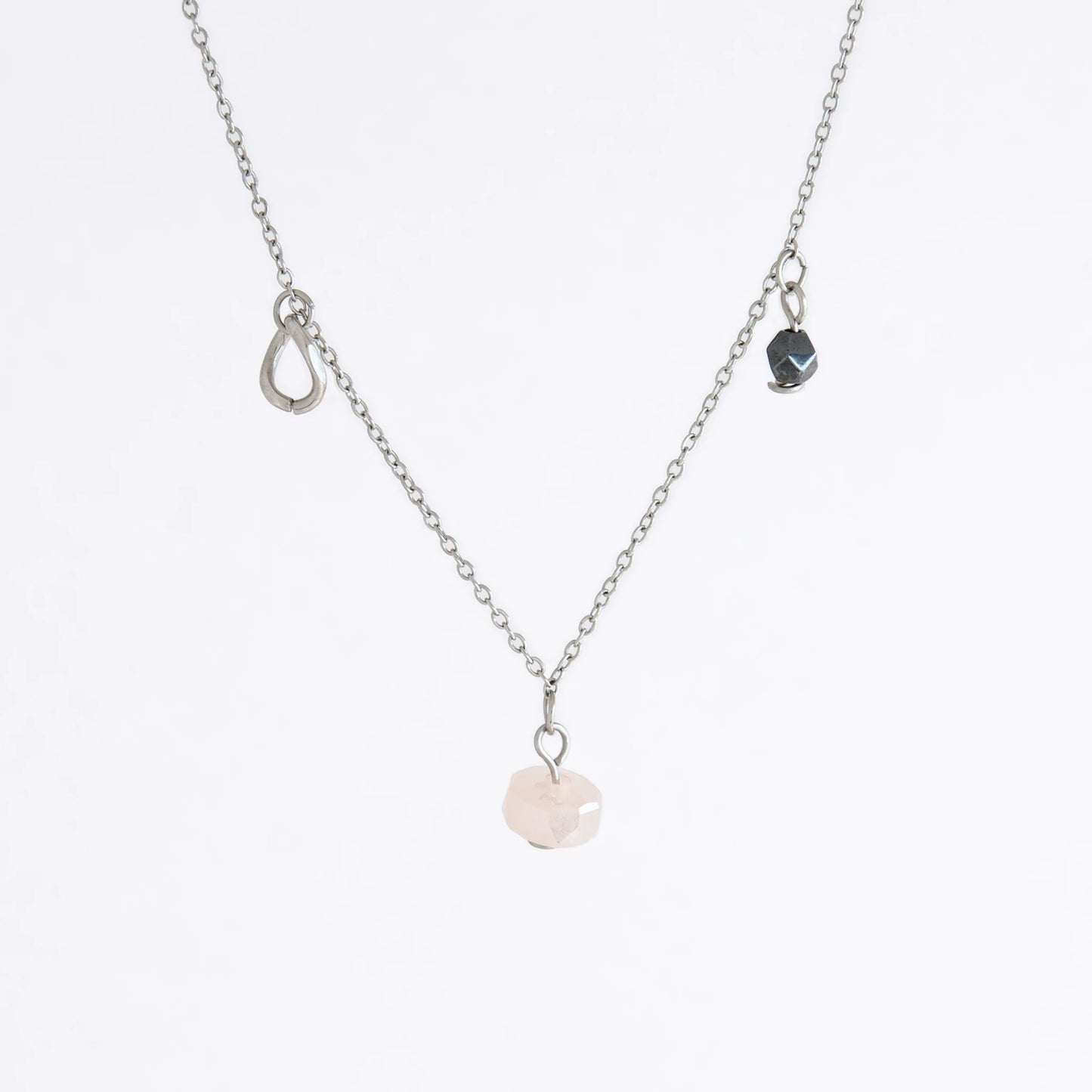 Silver stainless steel delicate charm necklace with small pink, black, purple glass beads and a geometric charm on a light gray background