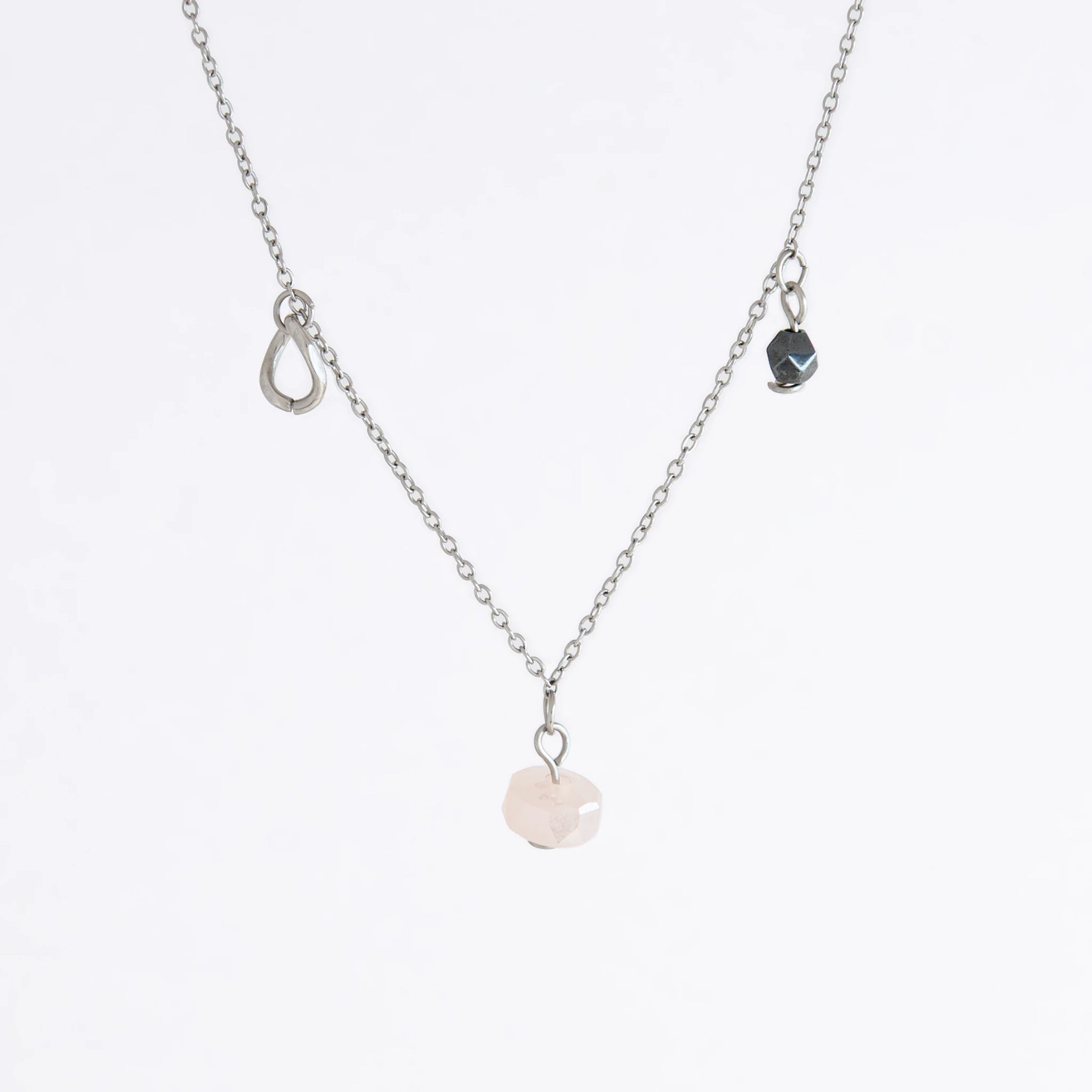 Silver stainless steel delicate charm necklace with small pink, black, purple glass beads and a geometric charm on a light gray background