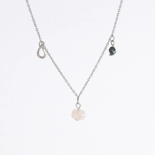 Silver stainless steel delicate charm necklace with small pink, black, purple glass beads and a geometric charm on a light gray background