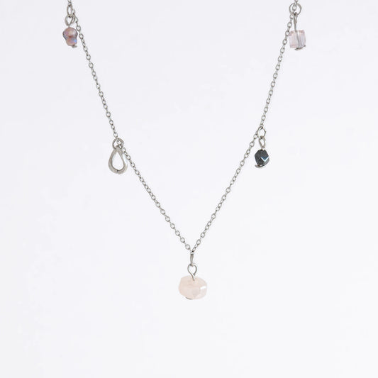 Silver stainless steel delicate charm necklace with small pink, black, purple glass beads and a geometric charm on a light gray background
