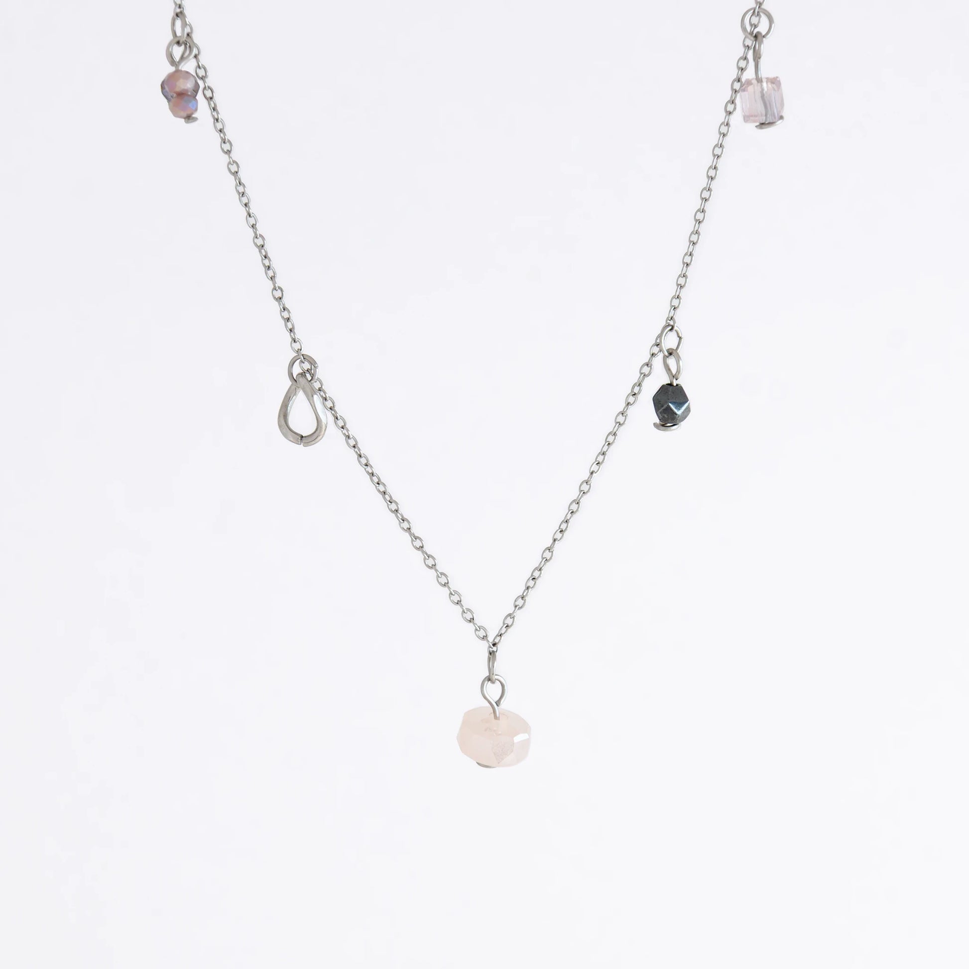 Silver stainless steel delicate charm bracelet with small pink, black, purple glass beads and a geometric charm on a light gray background