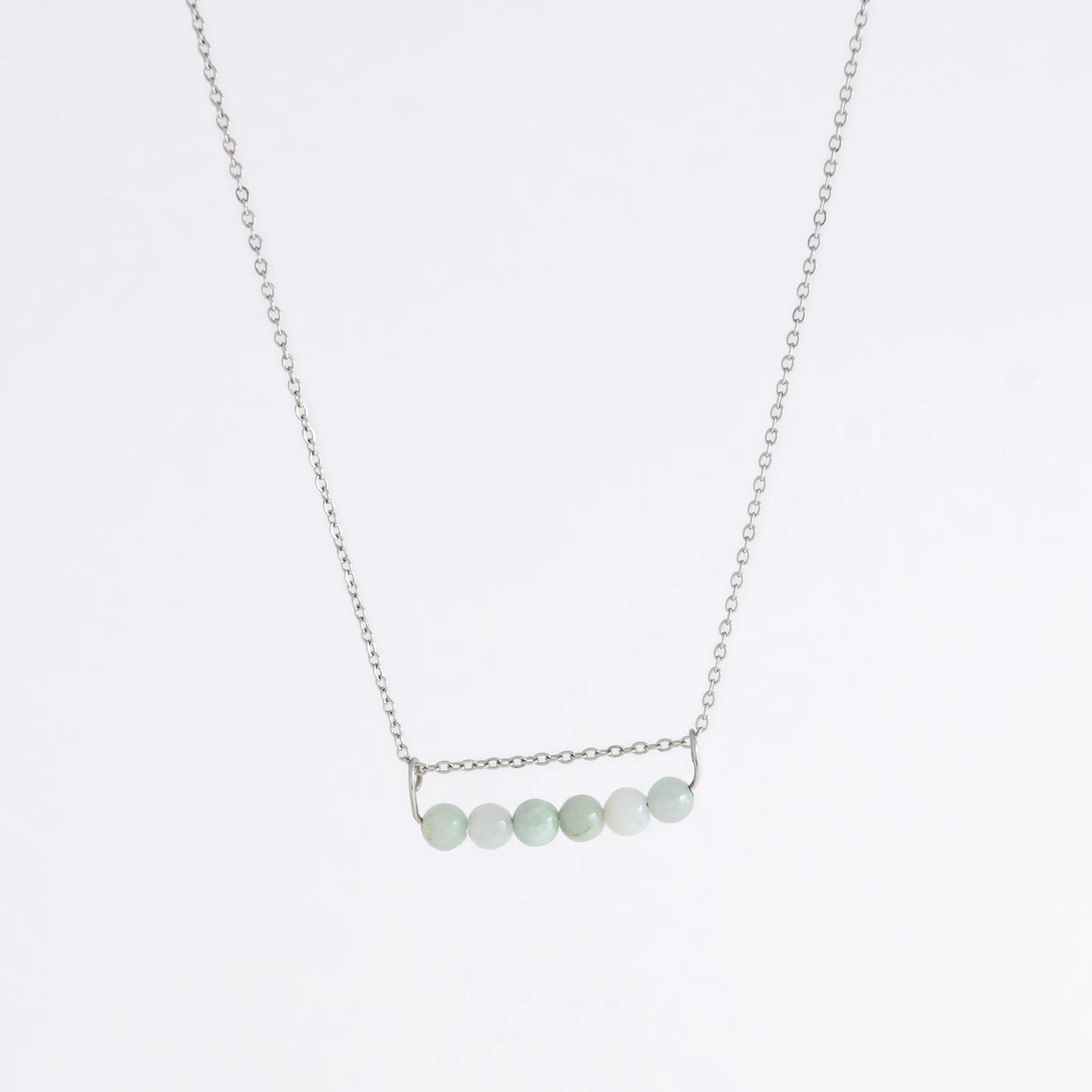 Silver necklace with a pendant made of jade beads on a light gray background