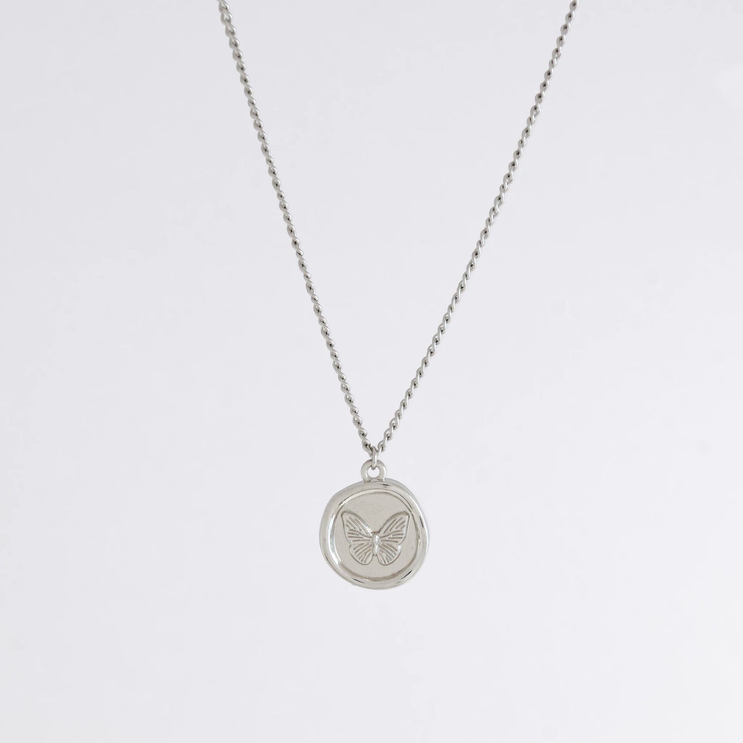 Silver curb necklace with a round butterfly pendant on a light gray background