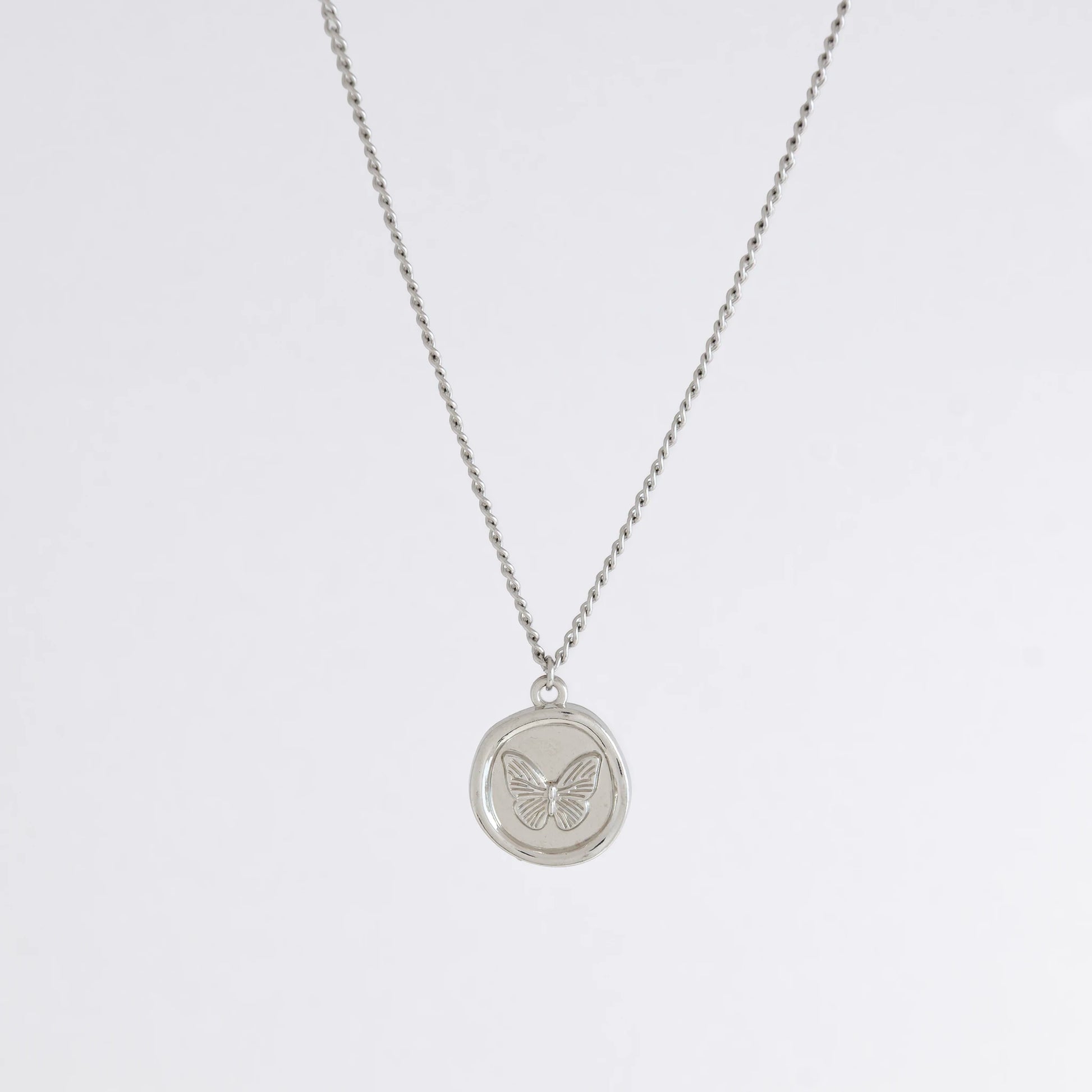 Silver curb necklace with a round butterfly pendant on a light gray background
