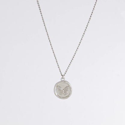 Silver curb necklace with a round butterfly pendant on a light gray background