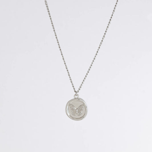 Silver curb necklace with a round butterfly pendant on a light gray background