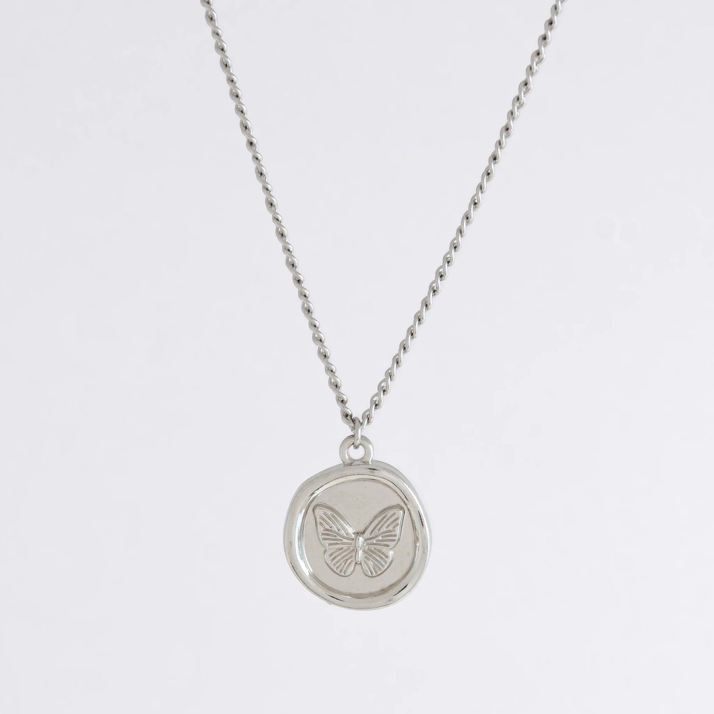 Silver curb necklace with a round butterfly pendant on a light gray background