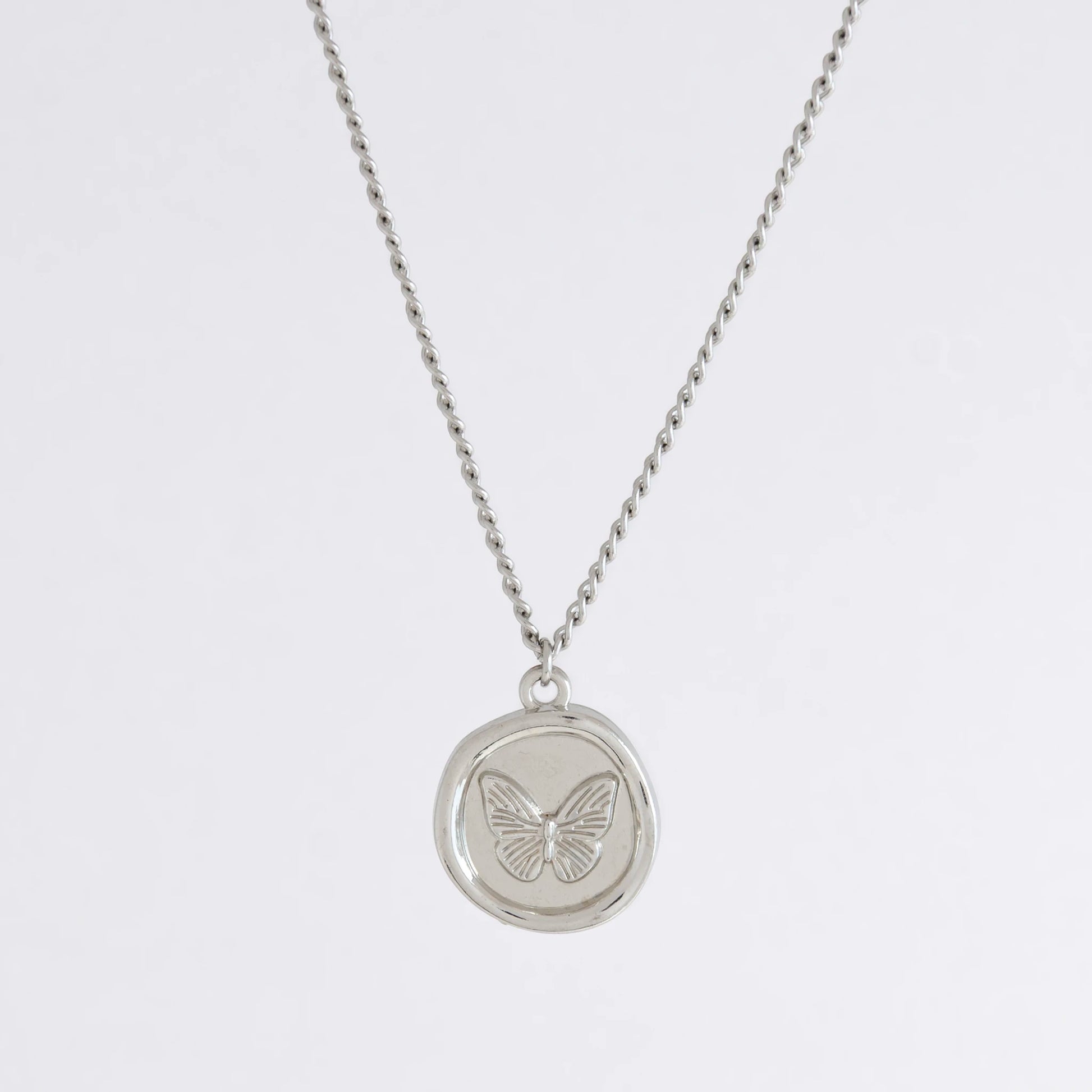 Silver curb necklace with a round butterfly pendant on a light gray background