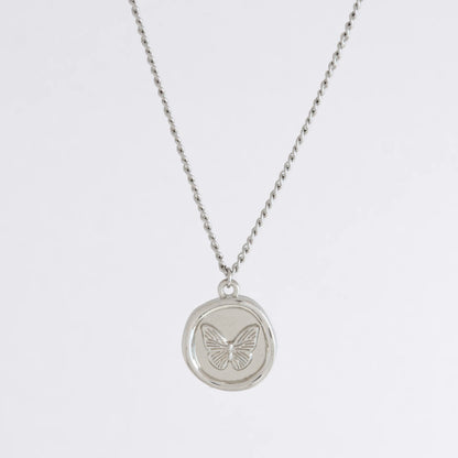 Silver curb necklace with a round butterfly pendant on a light gray background
