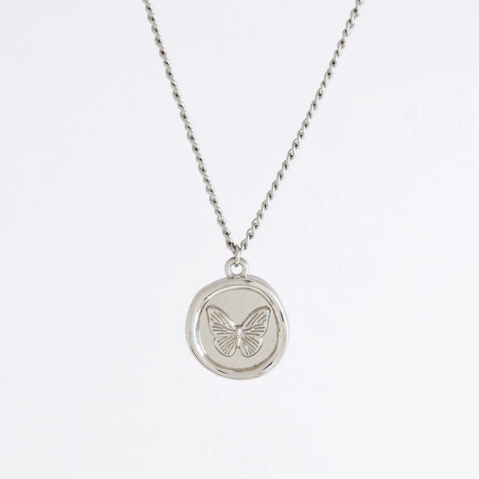 Silver curb necklace with a round butterfly pendant on a light gray background