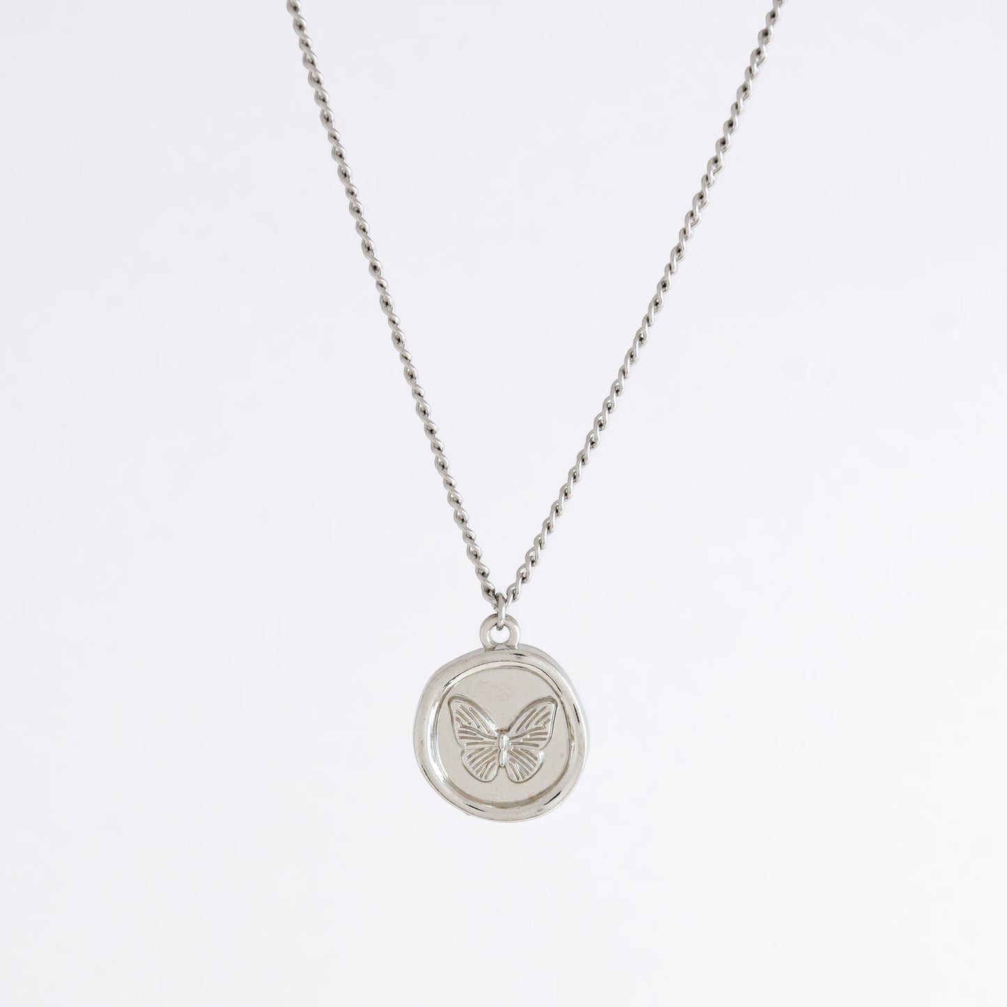 Silver curb necklace with a round butterfly pendant on a light gray background