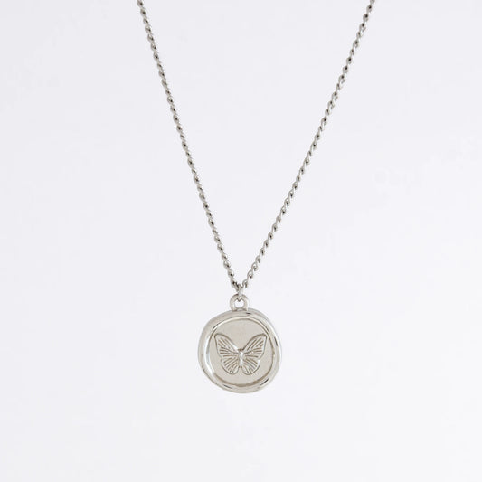 Silver curb necklace with a round butterfly pendant on a light gray background