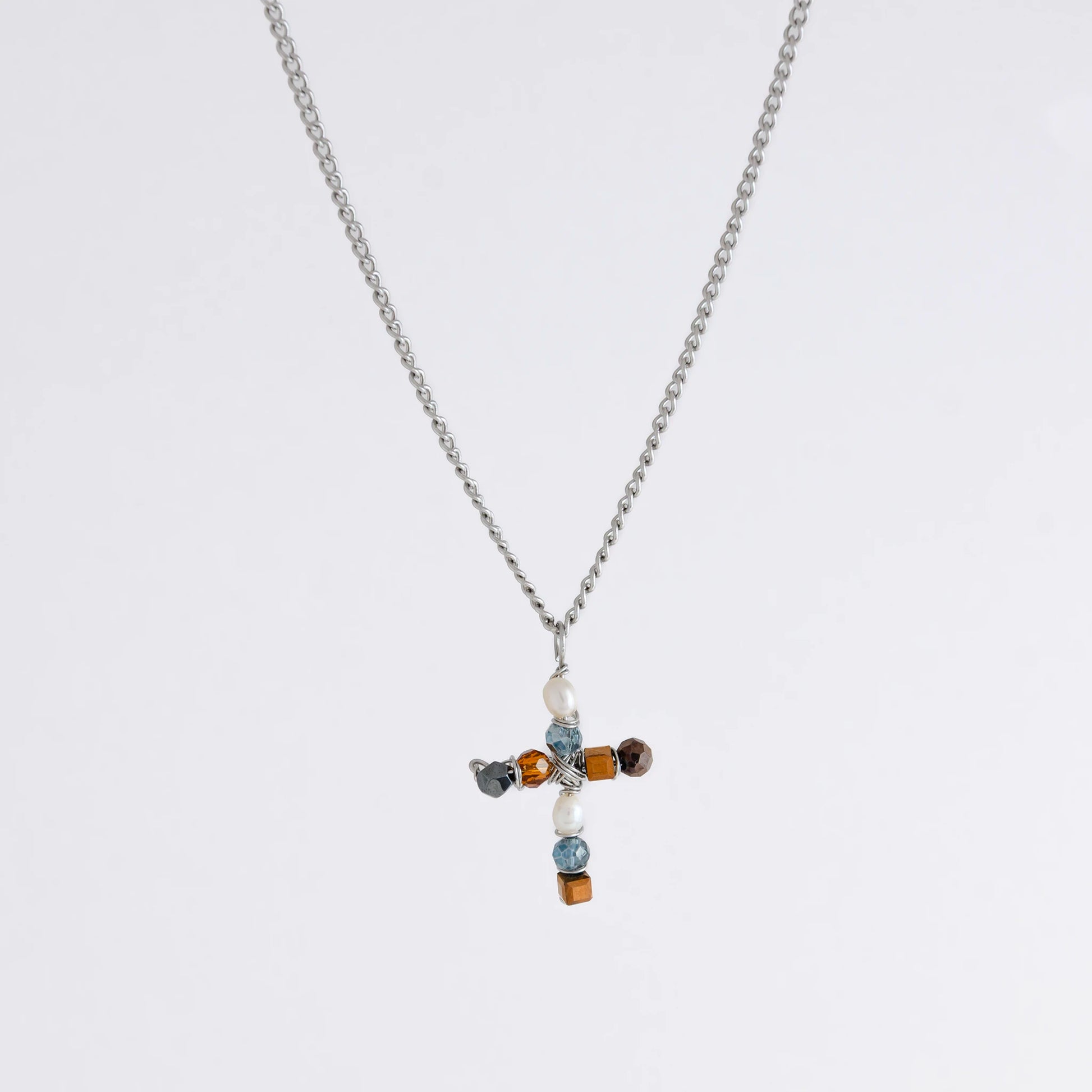 Silver curb chain necklace with a cross pendant made of freshwater pearls and blue, orange and black glass beads on a light gray background