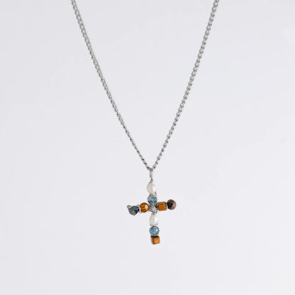 Silver curb chain necklace with a cross pendant made of freshwater pearls and blue, orange and black glass beads on a light gray background