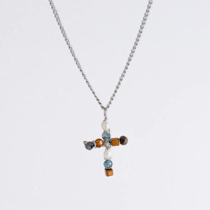 Silver curb chain necklace with a cross pendant made of freshwater pearls and blue, orange and black glass beads on a light gray background