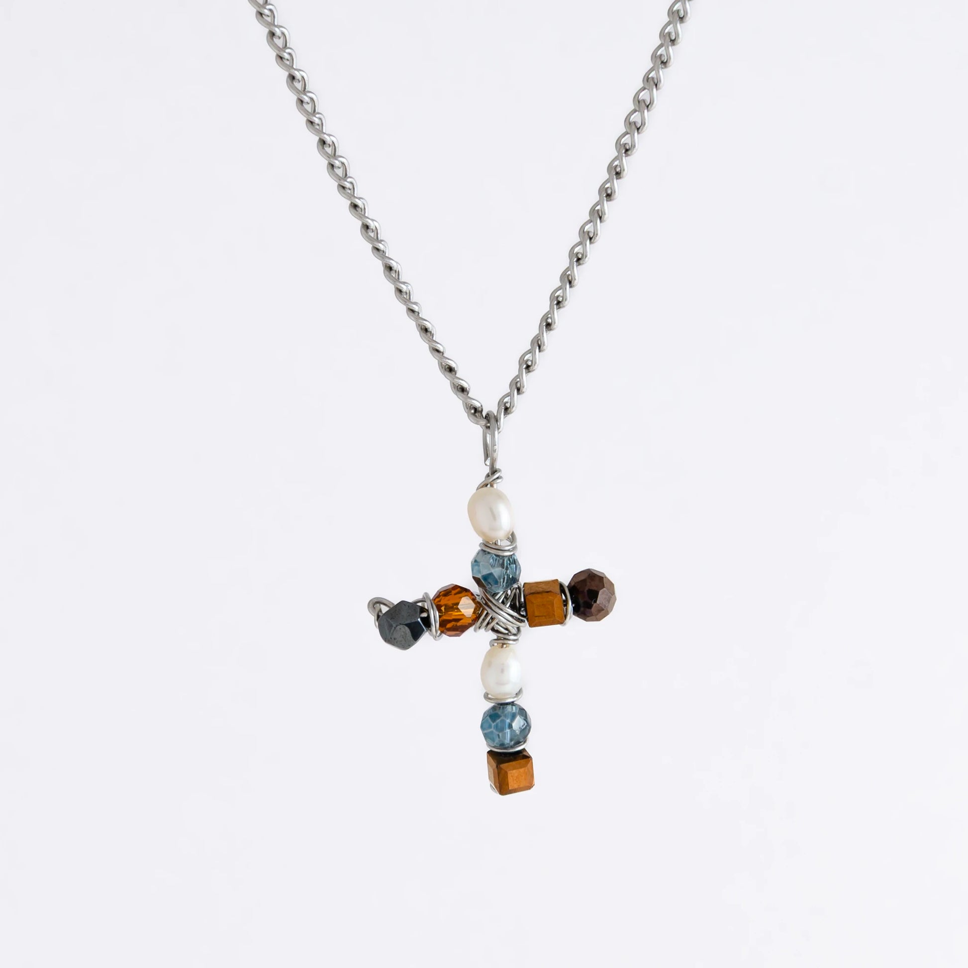 Silver curb chain necklace with a cross pendant made of freshwater pearls and blue, orange and black glass beads on a light gray background