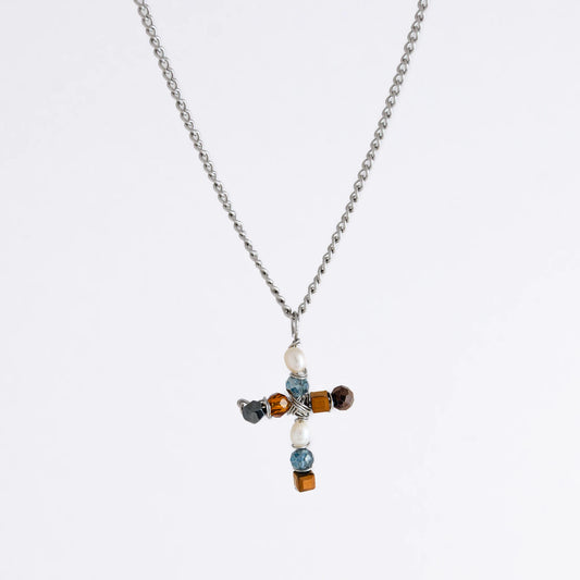 Silver curb chain necklace with a cross pendant made of freshwater pearls and blue, orange and black glass beads on a light gray background