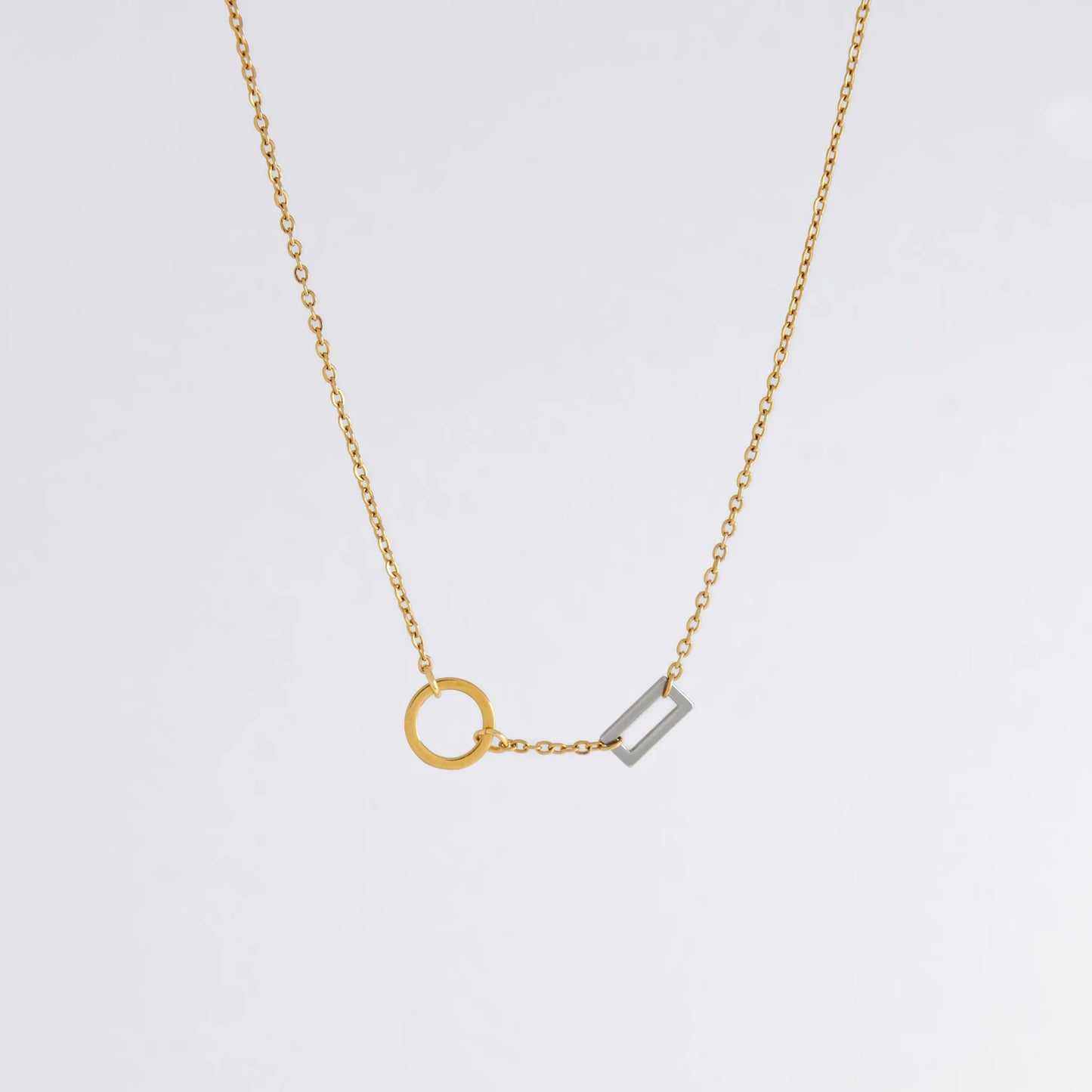 A gold chain necklace with a geometric design featuring a circle of brushed gold and a polished silver bar charm.