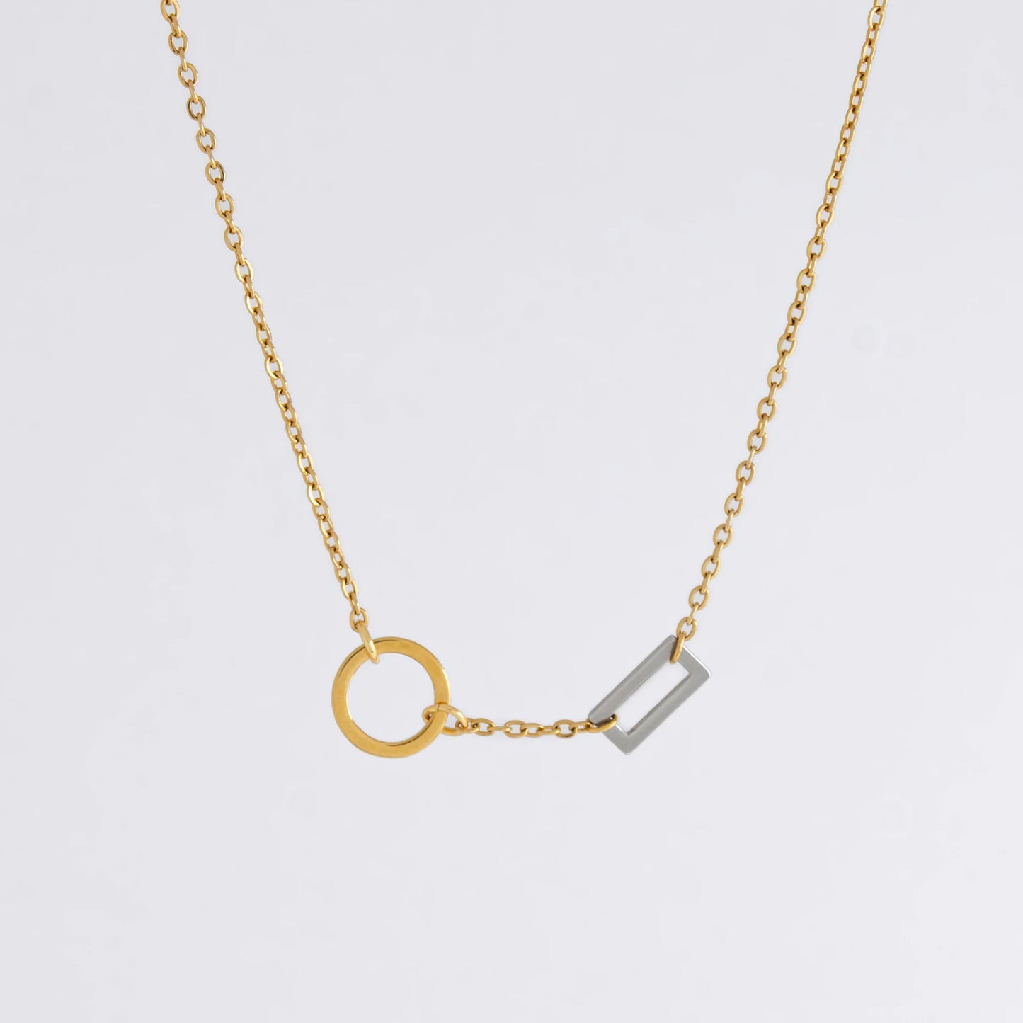 A gold chain necklace with a geometric design featuring a circle of brushed gold and a polished silver bar charm.