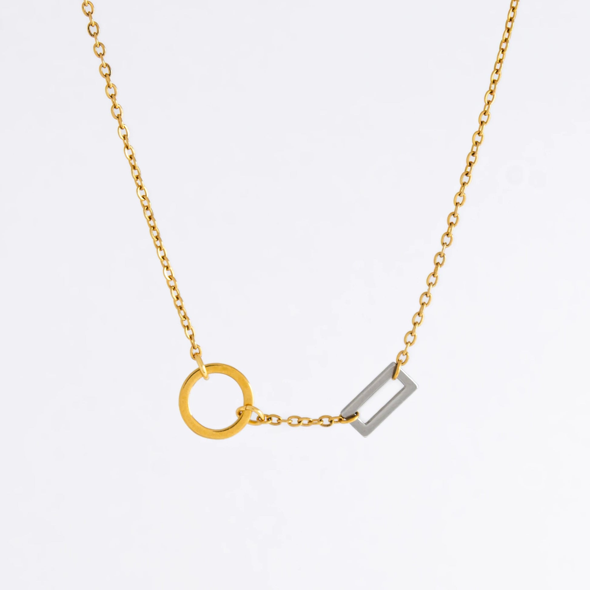 A gold chain necklace with a geometric design featuring a circle of brushed gold and a polished silver bar charm.