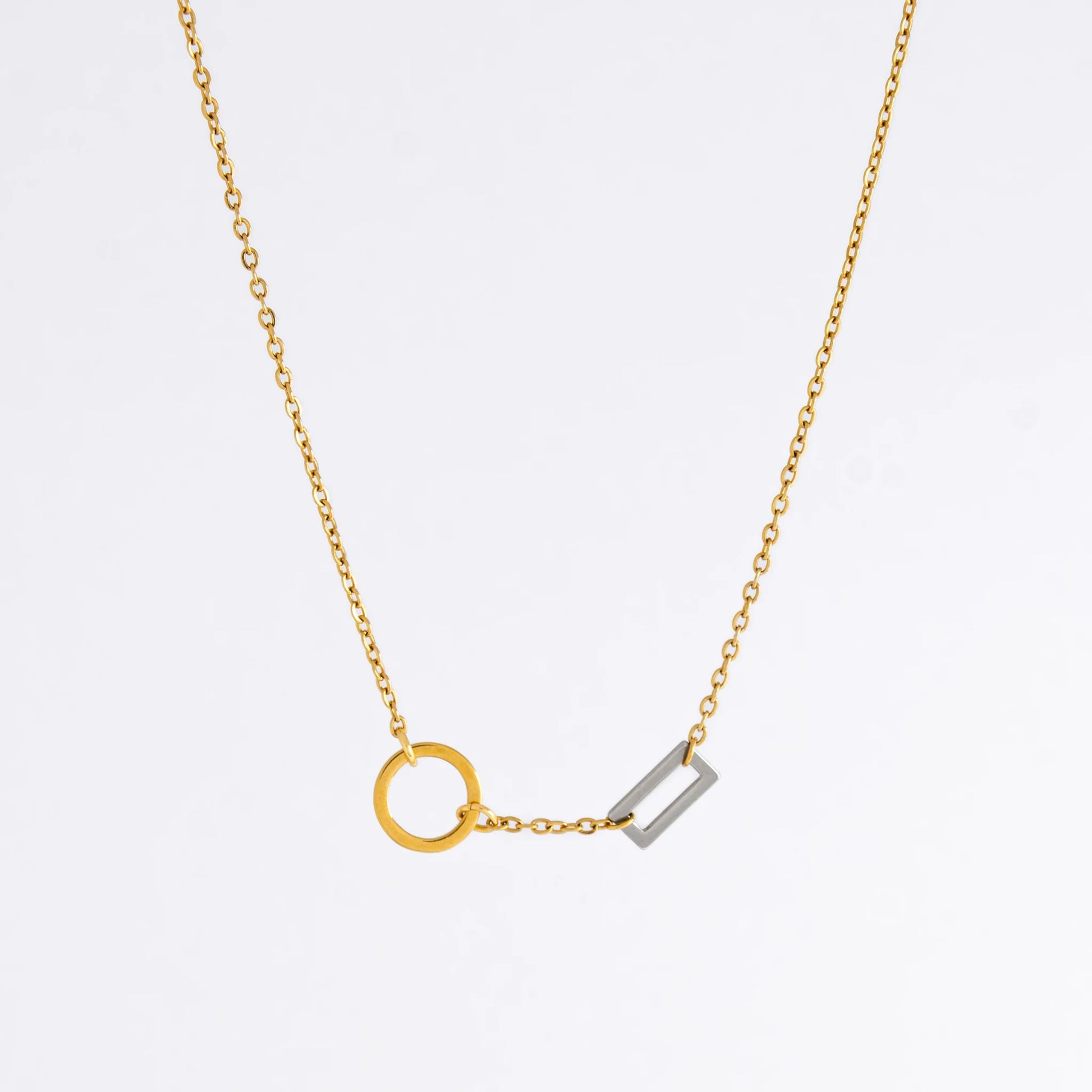 A gold chain necklace with a geometric design featuring a circle of brushed gold and a polished silver bar charm.