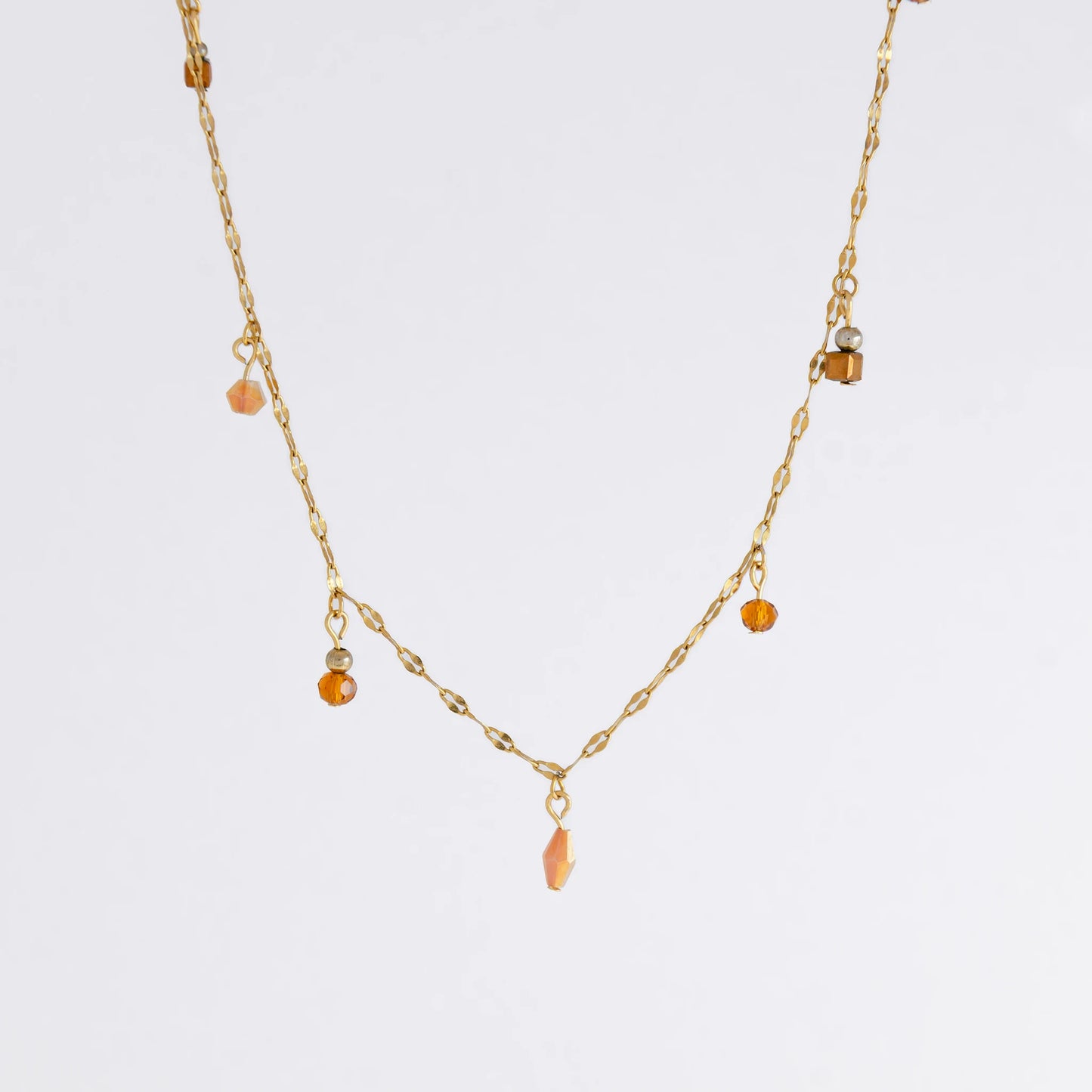 Delicate gold satellite necklace with small orange beads on a light gray background