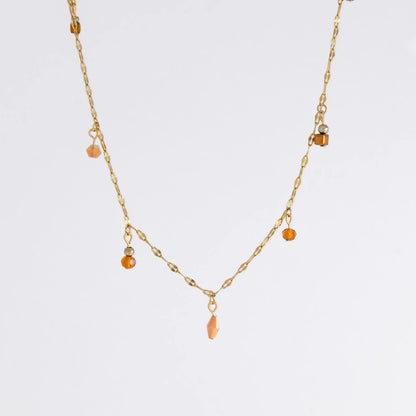 Delicate gold satellite necklace with small orange beads on a light gray background