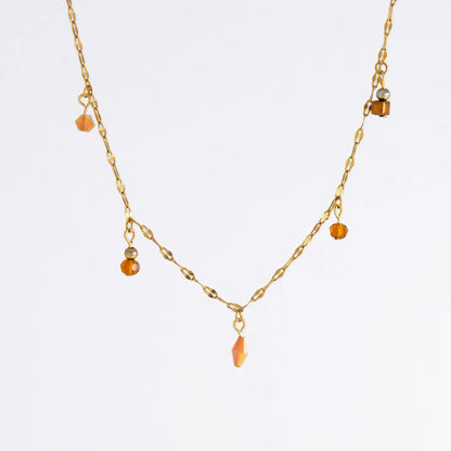 Delicate gold satellite necklace with small orange beads on a light gray background