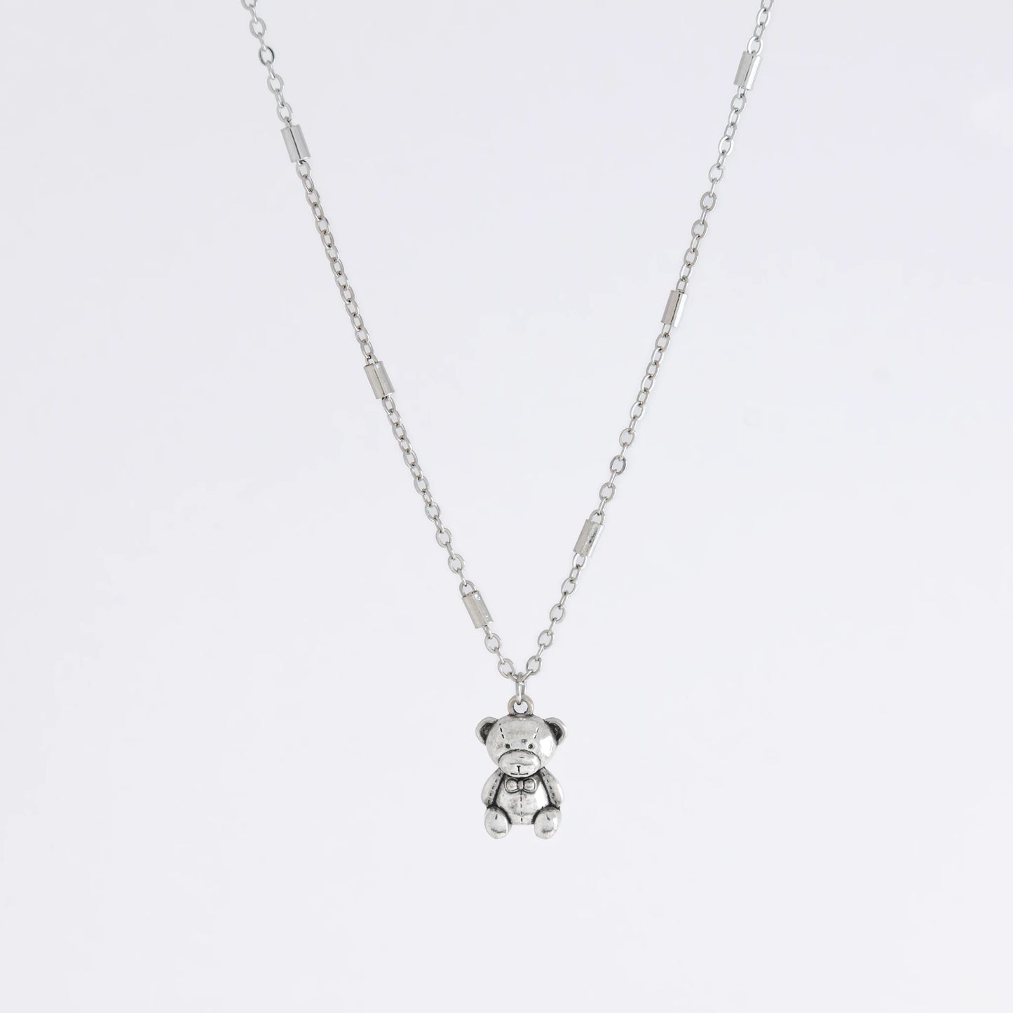 Dainty silver bar link chain with a teddy bear charm for minimalistic fashion or for layering jewelry on a light gray background