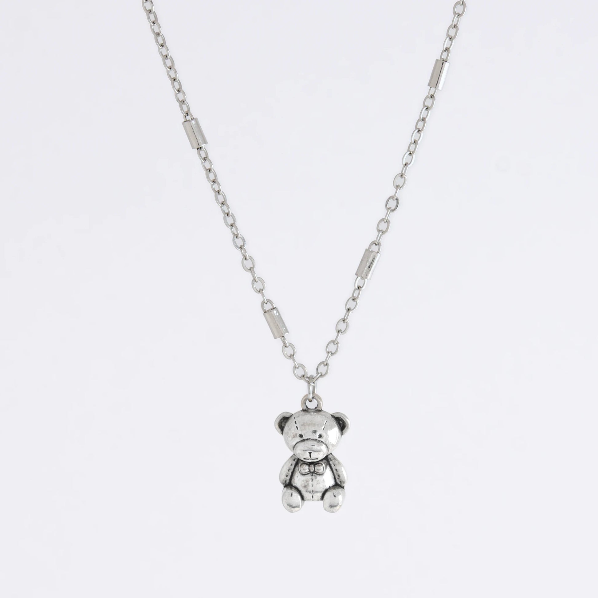 Dainty silver bar link chain with a teddy bear charm for minimalistic fashion or for layering jewelry on a light gray background