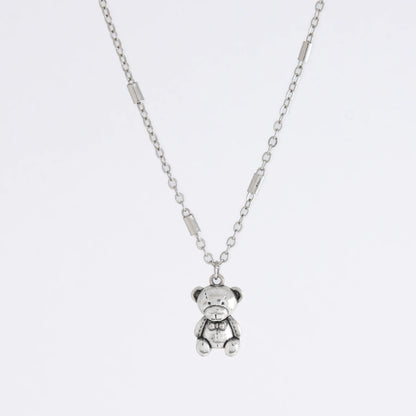 Dainty silver bar link chain with a teddy bear charm for minimalistic fashion or for layering jewelry on a light gray background