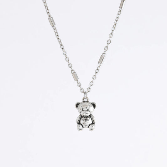 Dainty silver bar link chain with a teddy bear charm for minimalistic fashion or for layering jewelry on a light gray background